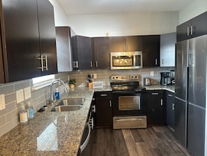 A modern kitchen with dark cabinetry, stainless steel appliances, granite countertops, and a built-in oven.