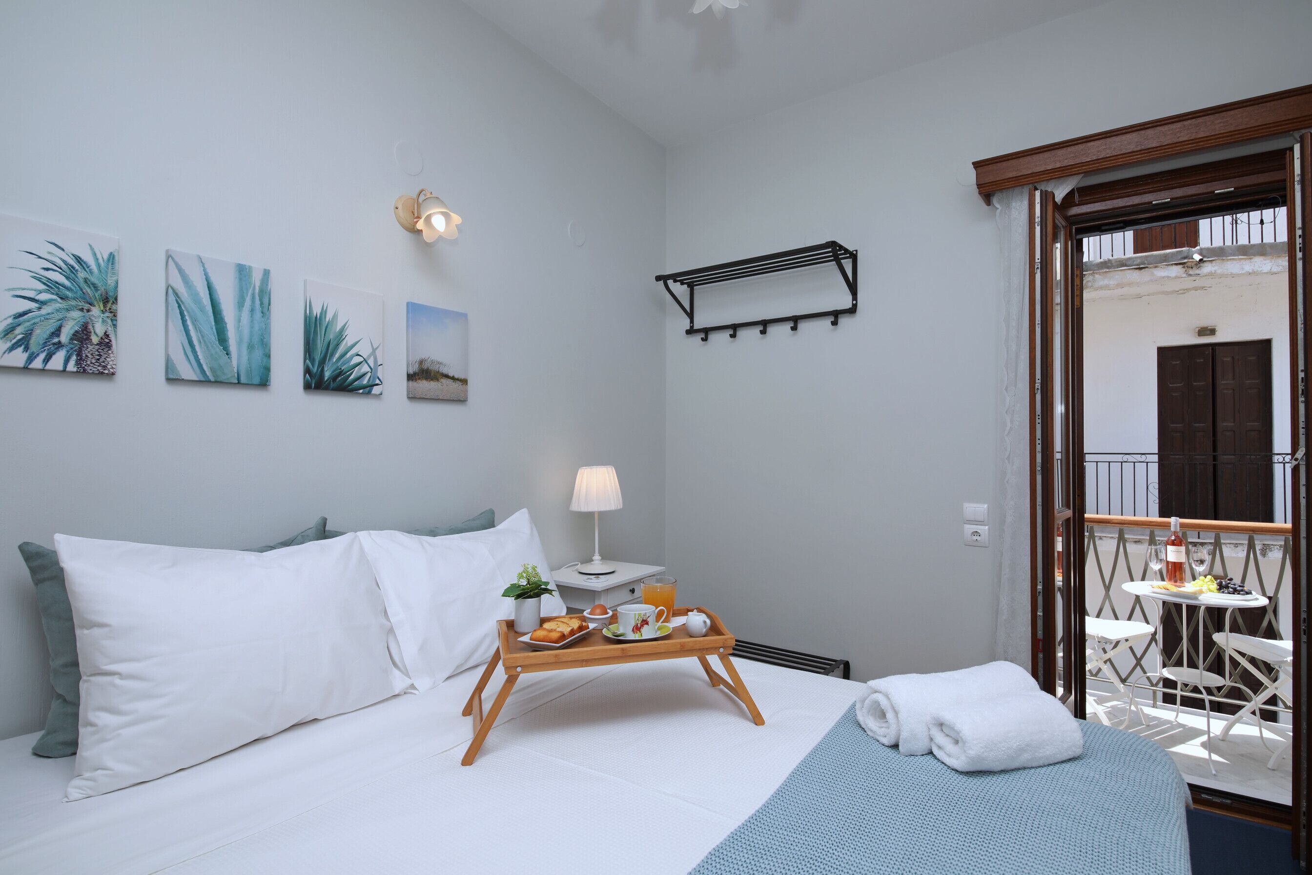 Une chambre d’hôtel avec un lit, une table de chevet avec une lampe, un plateau avec des articles pour le petit-déjeuner et un balcon avec une table et des chaises.