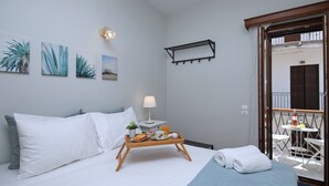 A hotel room with a bed, a bedside table with a lamp, a tray with breakfast items, and a balcony with a table and chairs.