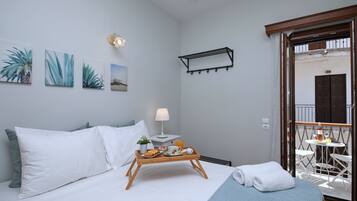 Une chambre d’hôtel avec un lit, une table de chevet avec une lampe, un plateau avec des articles pour le petit-déjeuner et un balcon avec une table et des chaises.