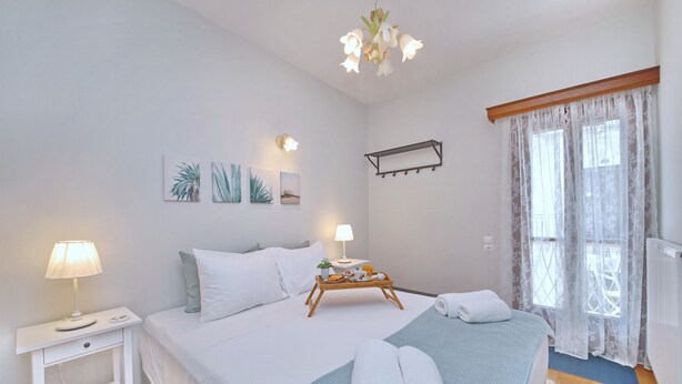 A neatly arranged bedroom with a bed, bedside tables, a hanging light fixture, and a window with sheer curtains.
