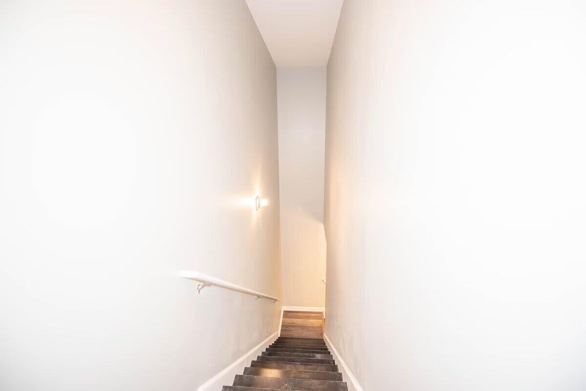 Un escalier étroit aux murs blancs, doté d’une rampe, menant à un palier.