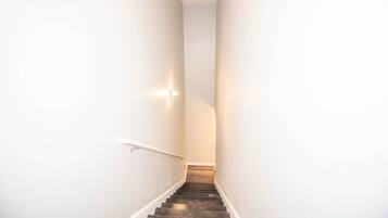 Un escalier étroit aux murs blancs, doté d’une rampe, menant à un palier.