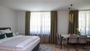 Een moderne hotelkamer met een groot bed, een zithoek met tafel en stoelen, en grote ramen voorzien van gordijnen.