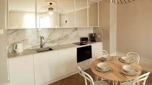 A modern kitchen with white cabinets, a marble countertop, and a dining area with a wooden table and white chairs. - Apartment in the Center (Gdansk)