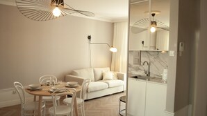 A modern dining area with a round table, white chairs, and a sofa. There is a kitchen with a marble countertop and a sink. - Apartment in the Center (Gdansk)