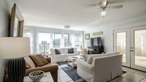 A living room with a white sofa, a coffee table, a TV, and a ceiling fan. - Dauphin Island's East End Jewl (Dauphin Island)