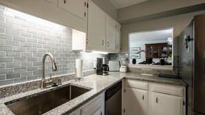 A kitchen with white cabinets, a granite countertop, a stainless steel sink, a coffee maker, and a refrigerator. - Dauphin Island's East End Jewl (Dauphin Island)