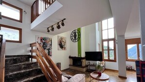 A spacious living area with a wooden staircase, a fireplace, a flat-screen TV, and a large window offering a mountain view. - Spacious house (sleeps 7) with incredible view HUT6007971 (Aubinyà)