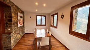 Un espace repas avec une table et des chaises en bois, des murs en pierre et de grandes fenêtres offrant une vue sur les montagnes.