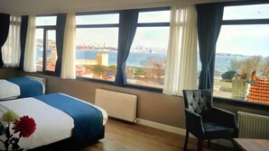 A hotel room with two beds, a view of the sea and cityscape, and a chair by the window. - Cape Palace Hotel (Istanbul)