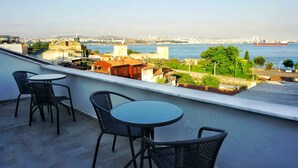 A balcony with two round tables and four chairs, overlooking a cityscape with buildings and a body of water. - Cape Palace Hotel (Istanbul)