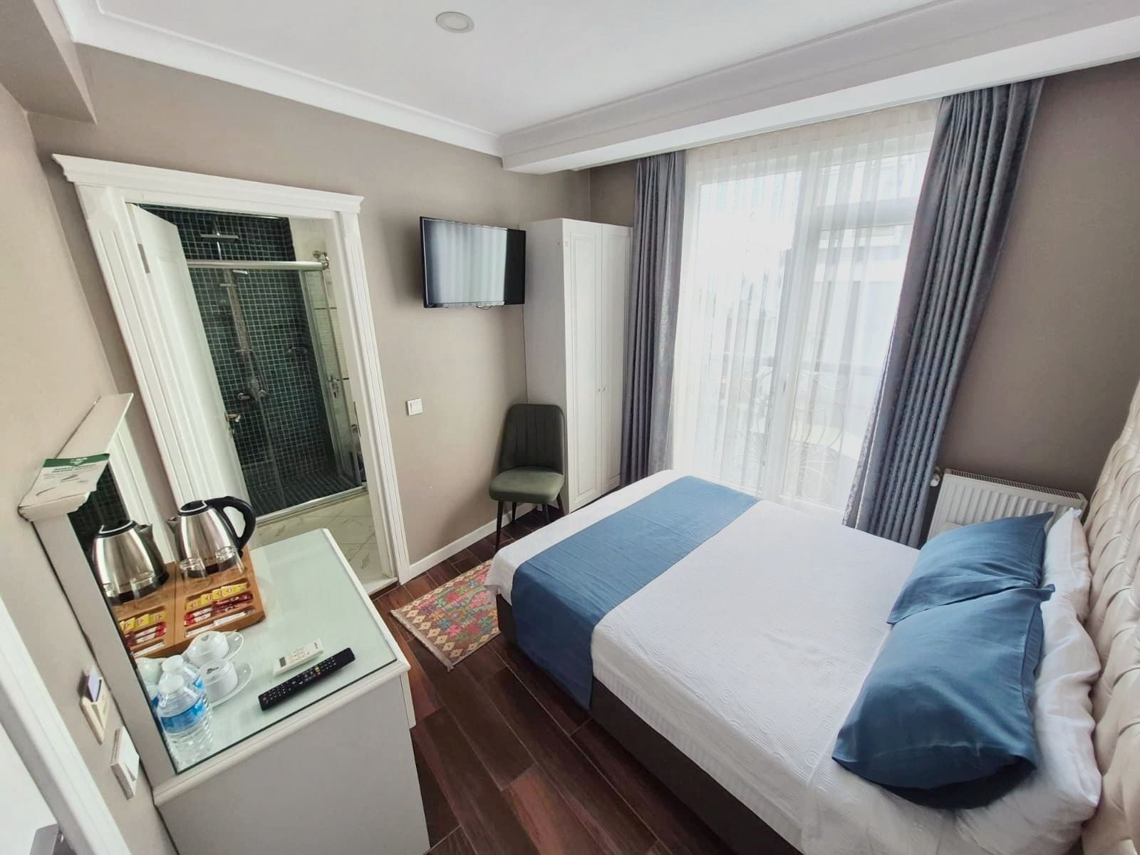 Hotelkamer met een bed, televisie, douche en een klein tafeltje met een waterkoker en waterflesjes.