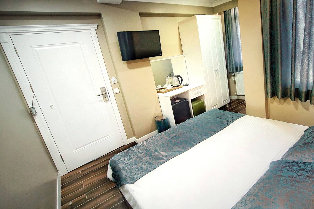 Quarto de hotel com cama, uma secretária com computador, televisão e guarda-roupa.