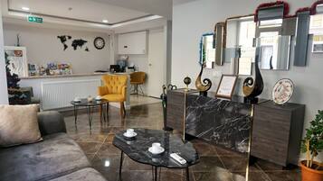 Un vestíbulo con un mostrador de recepción, un sillón amarillo, un sofá gris y una mesa de centro con tazas y un control remoto.