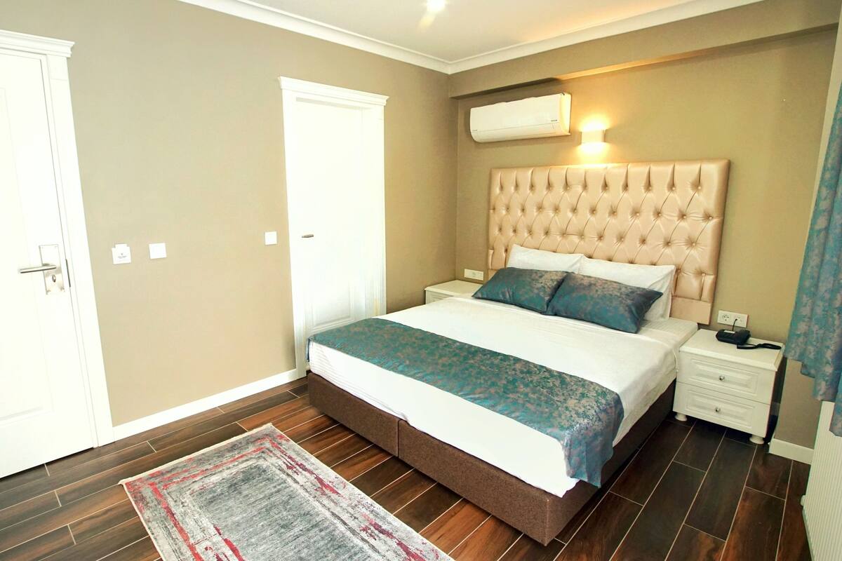 Quarto com uma cama grande, mesa de cabeceira, ar-condicionado fixado na parede e uma porta.