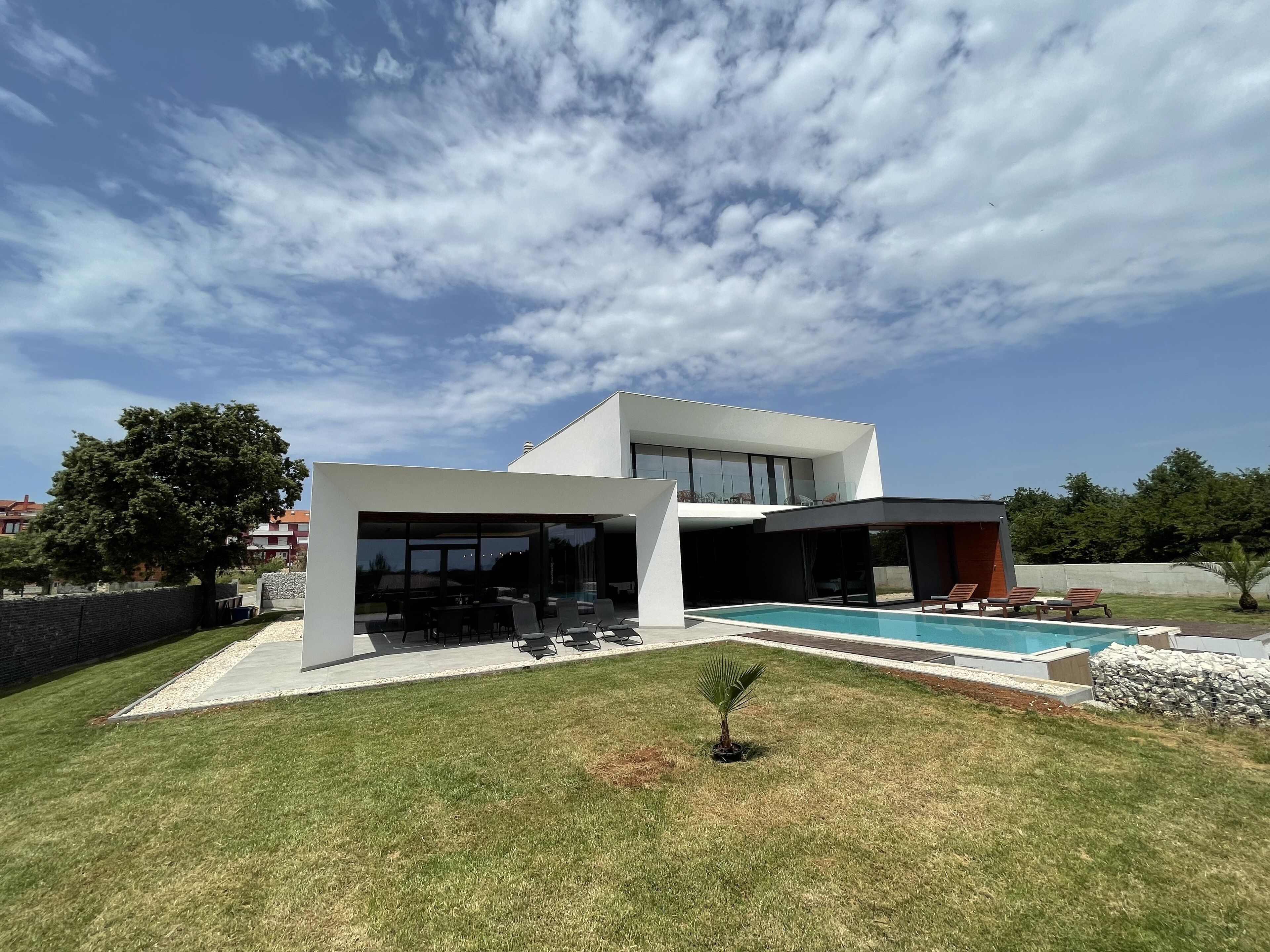 Une maison moderne dotée d’une piscine, d’un patio couvert et d’une pelouse bien entretenue.