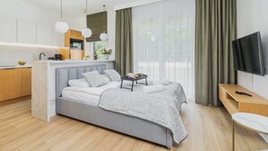 A modern bedroom with a bed, bedside table, TV, and a kitchen area with a microwave and sink. - Stylish Studio for Two with a Balcony | Close to the Old Town (Kraków)