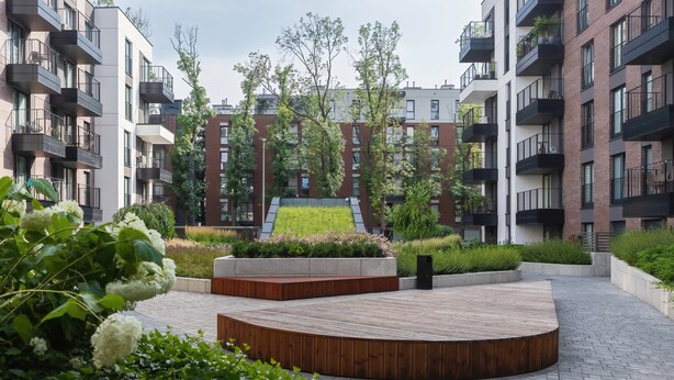 A modern apartment complex with balconies, a central green area, and a circular wooden platform. - Stylish Studio for Two with a Balcony | Close to the Old Town (Kraków)