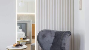 A modern room with a grey upholstered armchair, a round gold-framed side table with a plate of fruit, and a tall mirror reflecting the room's interior. - Stylish Studio for Two with a Balcony | Close to the Old Town (Kraków)