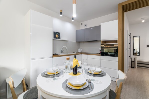 A modern kitchen with white cabinets, a dining table set for four with yellow napkins, and a cork bottle.