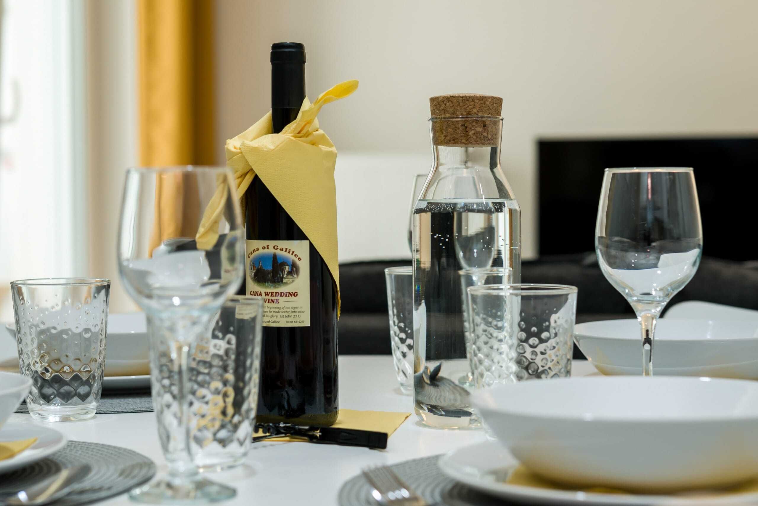 Uma mesa posta para refeição, com uma garrafa de vinho, copos e uma garrafa de água.