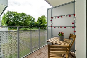 A balcony with a wooden table and chairs, a potted plant, and a decorative wall with red and white spherical ornaments. - Functional Apartment | Balcony, Parking, Close to Malta Lake (Poznan)