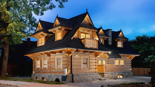 Ein blockhausartiges Haus mit vielen Fenstern und einem Steinfundament, das sich durch eine markante Veranda und einen gut beleuchteten Eingang auszeichnet.