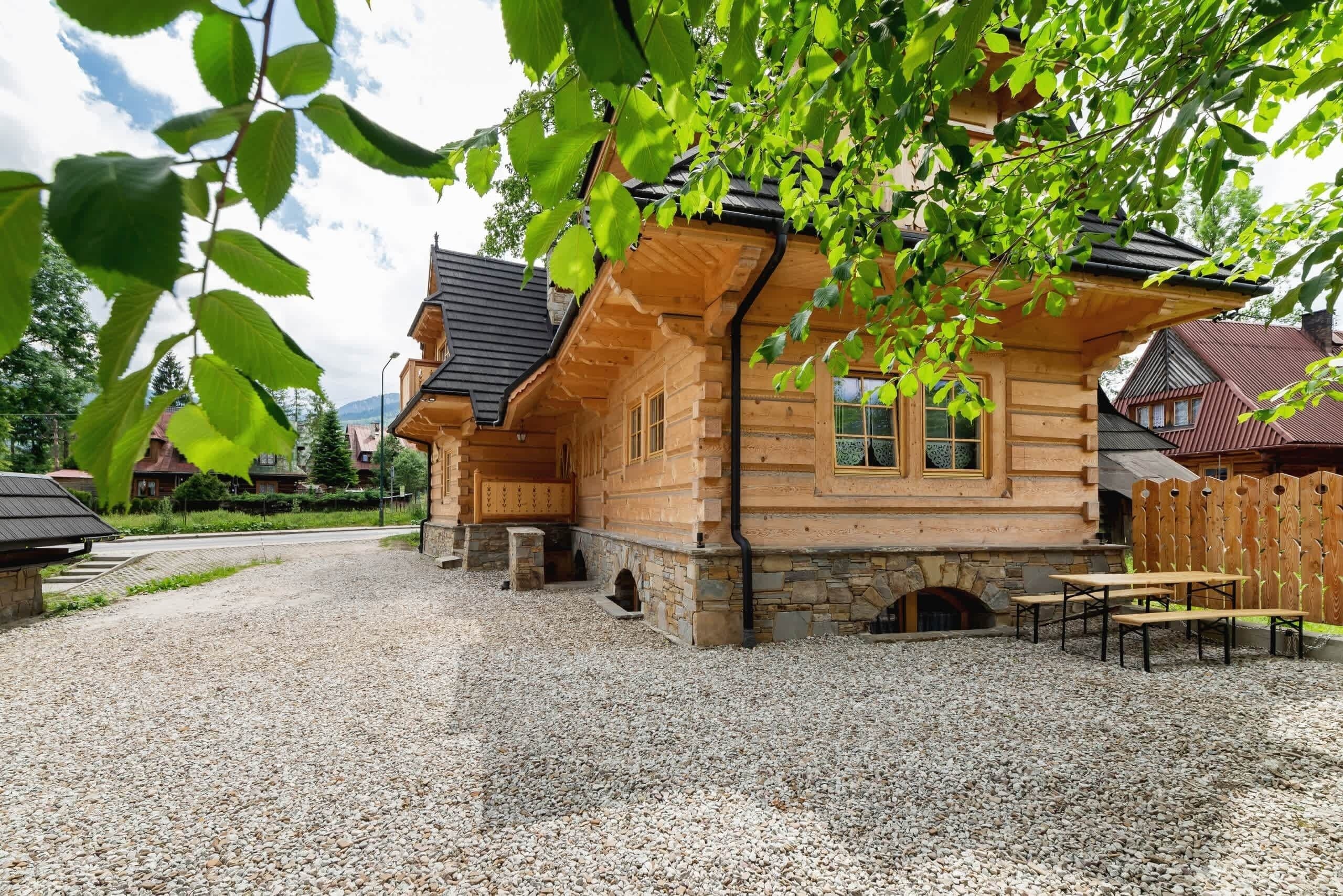 Een houten chalet met een stenen fundering, een grindpad en een houten omheining.