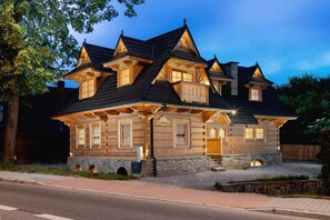 Una casa tipo cabaña de troncos con varias ventanas y cimientos de piedra, que destaca por un porche amplio y una entrada bien iluminada.