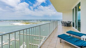 A balcony with a view of the sea, a dining area with chairs and a table, and a clear sky.