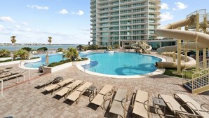 A resort pool area with a large pool, lounge chairs, and a water slide.