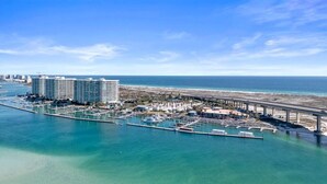 An aerial view of a coastal marina with a large hotel, a pier, and a beach in the background.