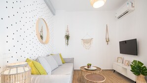 Ein modernes Wohnzimmer mit einem grauen Sofa, einem runden Spiegel, einem kleinen runden Tisch und einer großen Küsterpflanze.