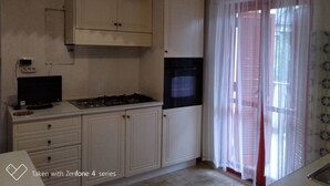 Une cuisine avec des meubles blancs, une cuisinière, un four noir et un téléviseur.
