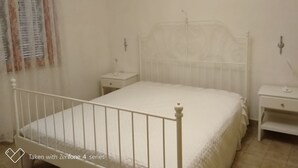Un lit à baldaquin blanc avec deux tables de chevet assorties, une fenêtre avec des rideaux et une lampe fixée au mur.