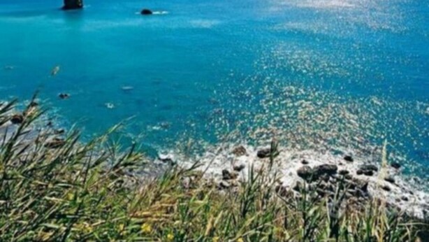 Un paysage côtier caractérisé par une eau turquoise et limpide, une côte rocheuse et des montagnes lointaines sous un ciel dégagé.