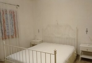 A white four-poster bed with matching nightstands, a window with curtains, and a wall-mounted lamp.