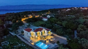 Una casa moderna de dos pisos con piscina, rodeada de árboles y vista al mar.