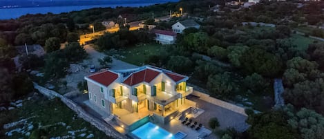 Uma casa moderna de dois andares com piscina, rodeada por árvores e vista para o mar.