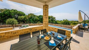Un área de comedor al aire libre con un muro de piedra, una piscina y vistas al mar.