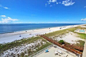 A beach with a wooden boardwalk, a pool area, and a view of the ocean.