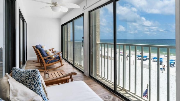 A balcony with a view of the beach, a ceiling fan, and a rocking chair. - Edgewater 41 (Gulf Shores)