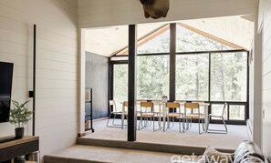 Un intérieur moderne avec une grande fenêtre, un coin repas avec des chaises et un téléviseur posé sur un meuble.