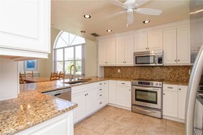 Enjoy cooking in this well-equipped kitchen with a large window, stainless steel appliances, and a ceiling fan for ventilation.
