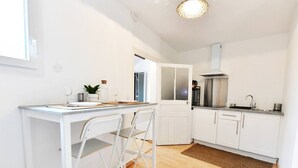 Une cuisine compacte avec des meubles blancs, une cuisinière encastrée et un petit coin repas comprenant une table et des chaises.