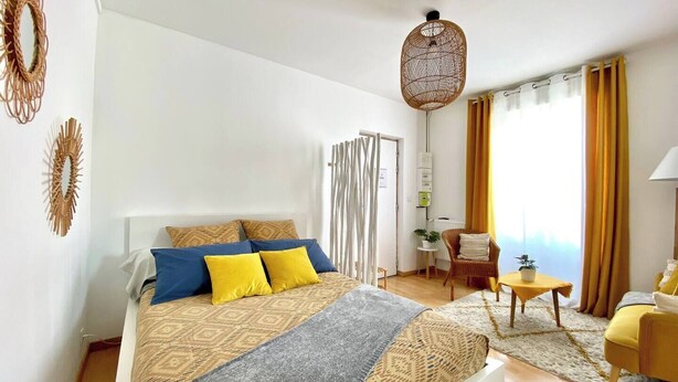 Une chambre moderne avec un grand lit, une petite table, une chaise et un luminaire suspendu.