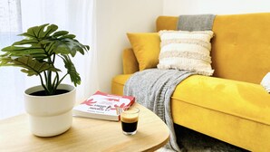 Un salon chaleureux avec un canapé jaune, une plante en pot blanche, une tasse de café et un livre posé sur une table en bois.