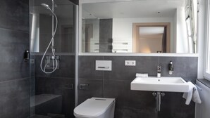 Een moderne badkamer met een douchecabine van glas, een wit toilet en een wastafel met een spiegel erboven.