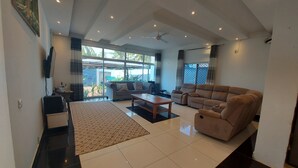A spacious living room with a large sofa, a coffee table, and a TV mounted on the wall. - Butterfly House (Malindi)